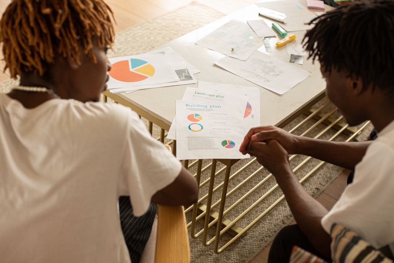 who-we-are Two men collaborating over building plans at a desk, discussing data charts.